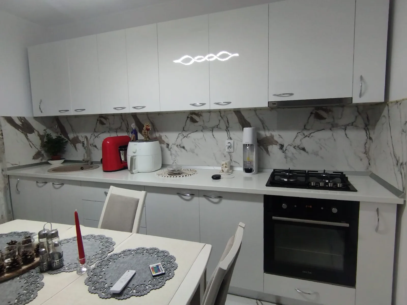 Bucătăria albă văzută din zona de masă, cu blat alb continuu